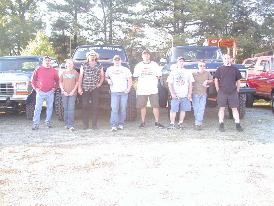 group of people standing in front of several lifted trucks