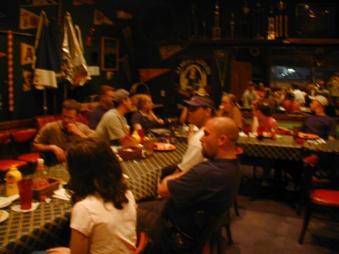 1988 Ford Bronco - A group of people are seated at tables in a dimly lit establishment, possibly a bar or restaurant, with trophies visible in the background.