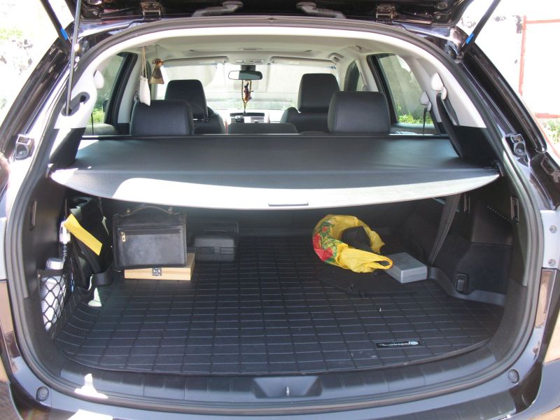 Open cargo area of a dark SUV with items on the floor mat and a cargo cover.