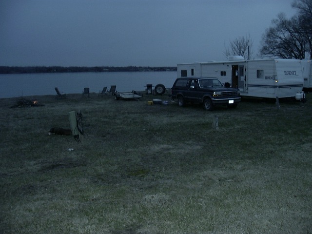 1992 Ford Bronco parked near a lake with two RVs and camping chairs