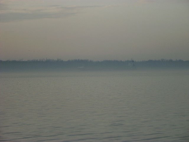 Water with a distant treeline under a hazy sky. SUPERMOTORS.NET logo in lower right