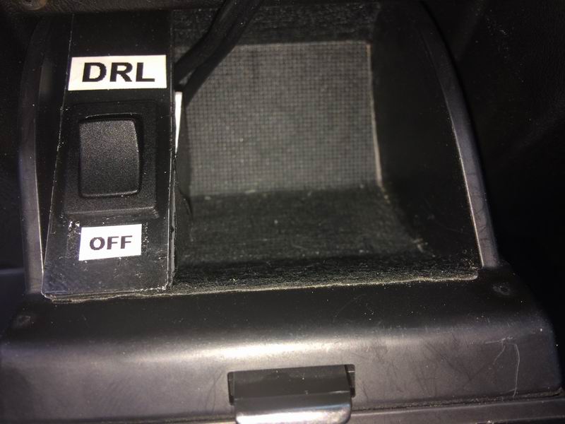 Close-up of DRL/OFF switch in a car's center console next to a storage compartment.