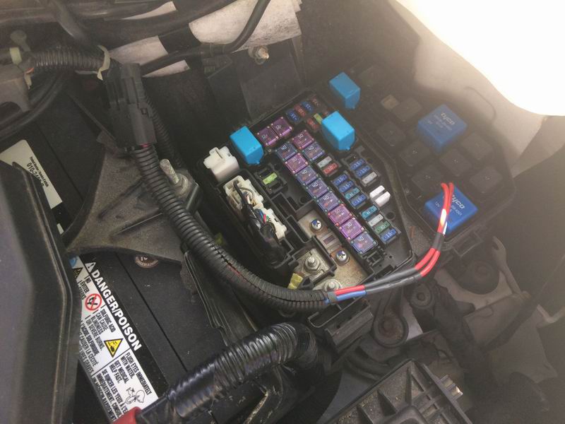 Car fuse box and battery with visible fuses, relays, and wiring.