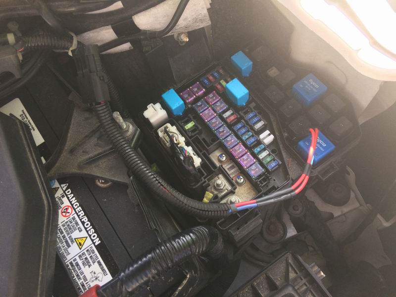 Close-up of car fuse box and battery with wires connected to a blue relay.
