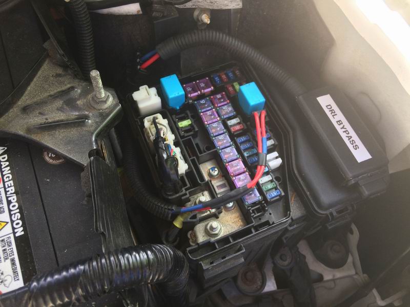 Close-up of a vehicle fuse box with DRL BYPASS label, battery, and wiring.