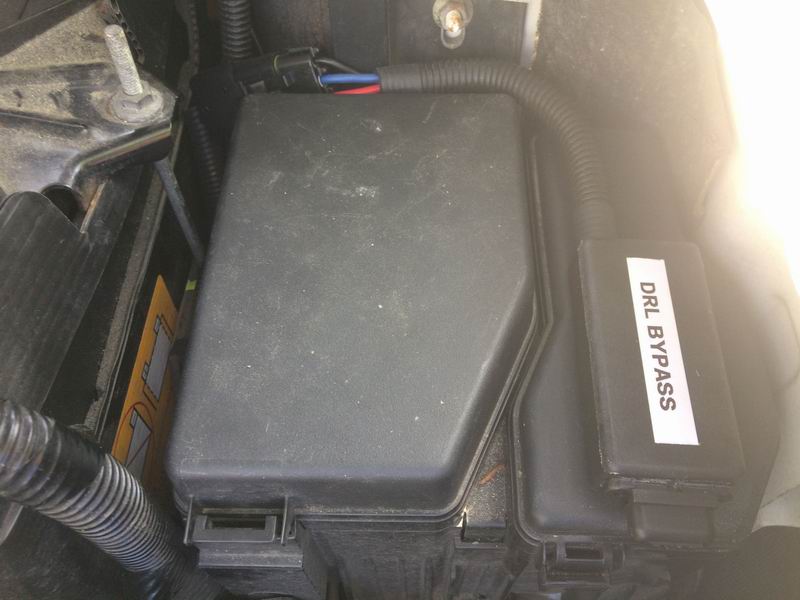 Close-up of a DRL bypass module attached to a vehicle fuse box.