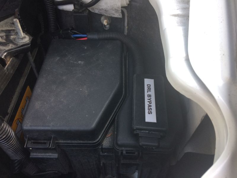 Close-up of a car fuse box with a DRL BYPASS module attached.