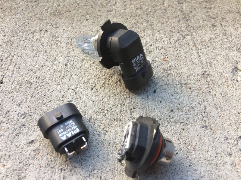 Three automotive light bulbs on concrete, two with PIAA branding.