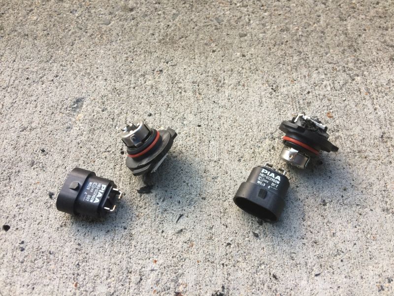 Two pairs of PIAA H3 bulbs on concrete, one pair disassembled.