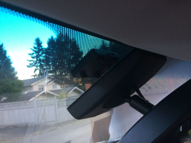 Interior view of car windshield with dashcam and houses outside.