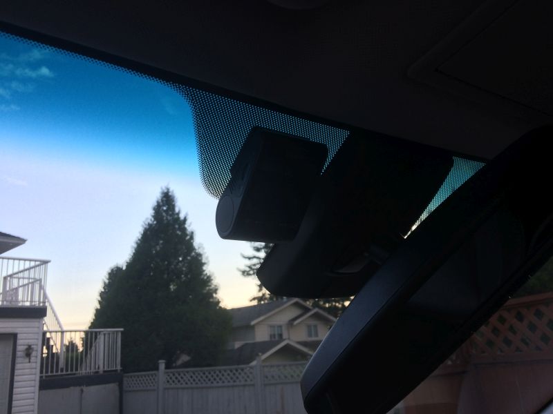 Dashcam mounted on a car windshield with view of houses and trees outside.
