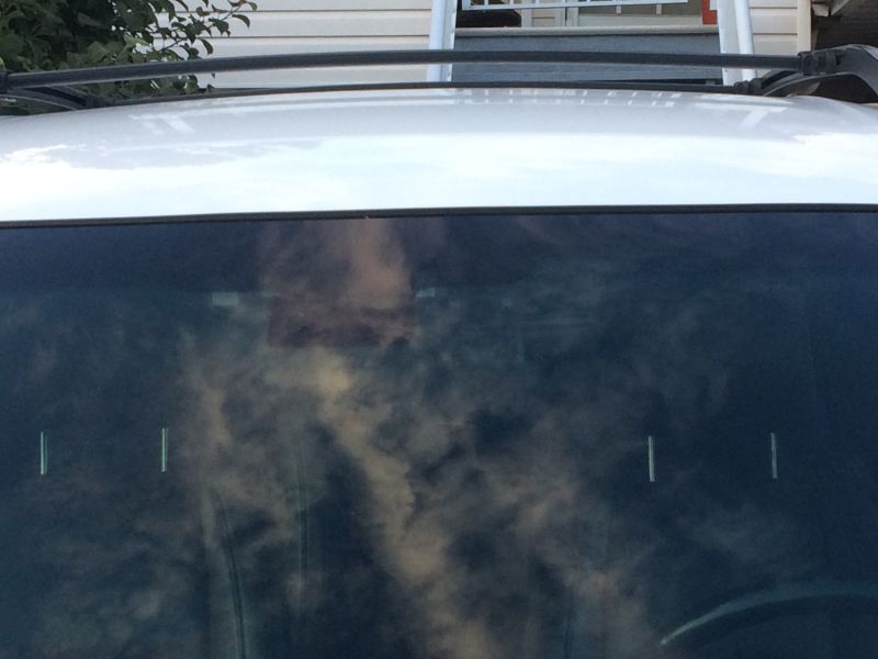 White SUV windshield reflecting clouds and a house, with vertical lines on the glass.