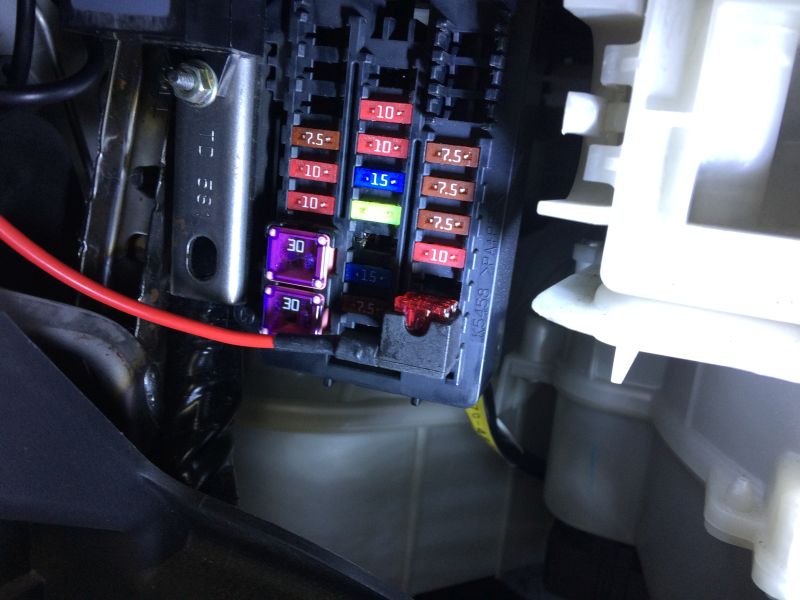 Close-up of car fuse box with purple and red fuses and a red wire.