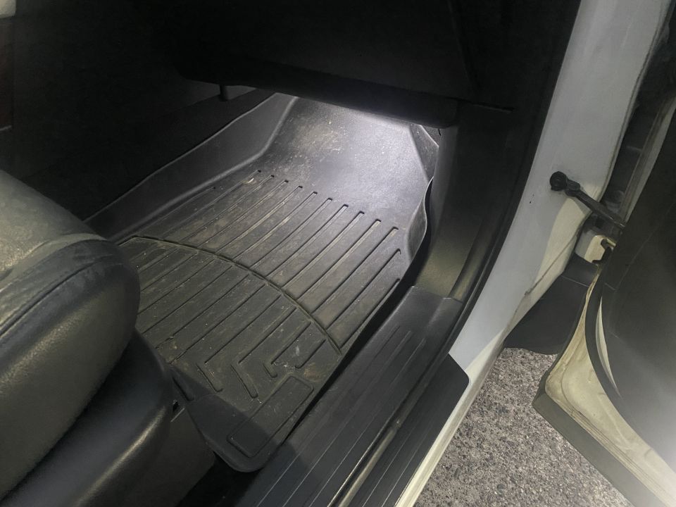 Close-up of a black rubber floor mat inside a vehicle, with a leather seat visible.
