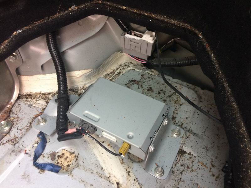 Silver electronic module with wires and conduit in a dirty vehicle trunk.