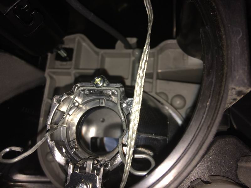 Headlight bulb retainer clip secured by a screw in a gray plastic housing.
