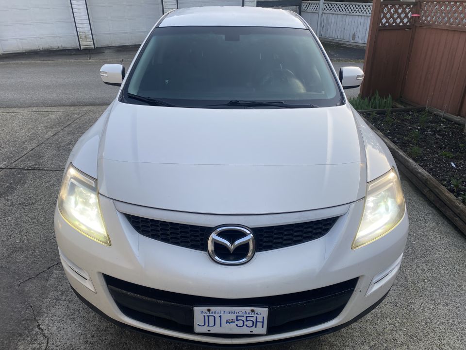 White 2009 Mazda CX-9 front view, headlights on, parked on driveway.