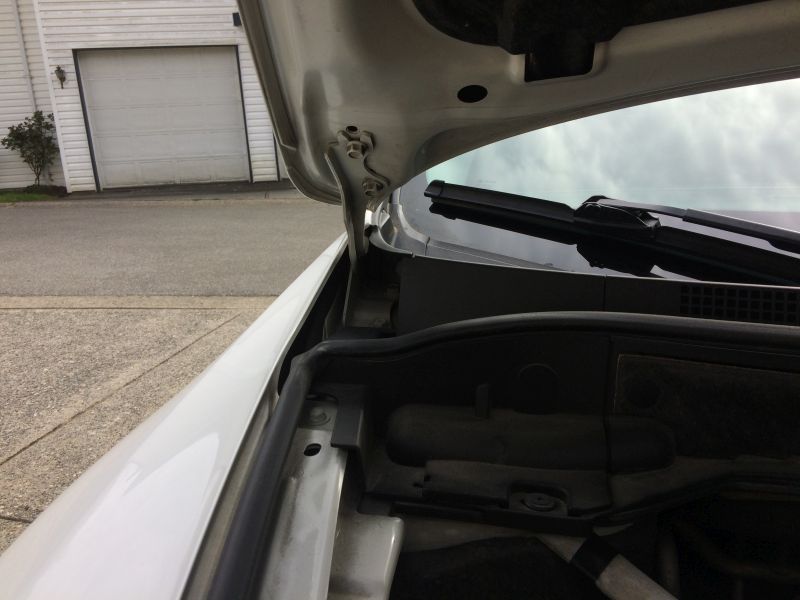 White car hood open, showing hinges and engine bay. Garage and driveway in background.