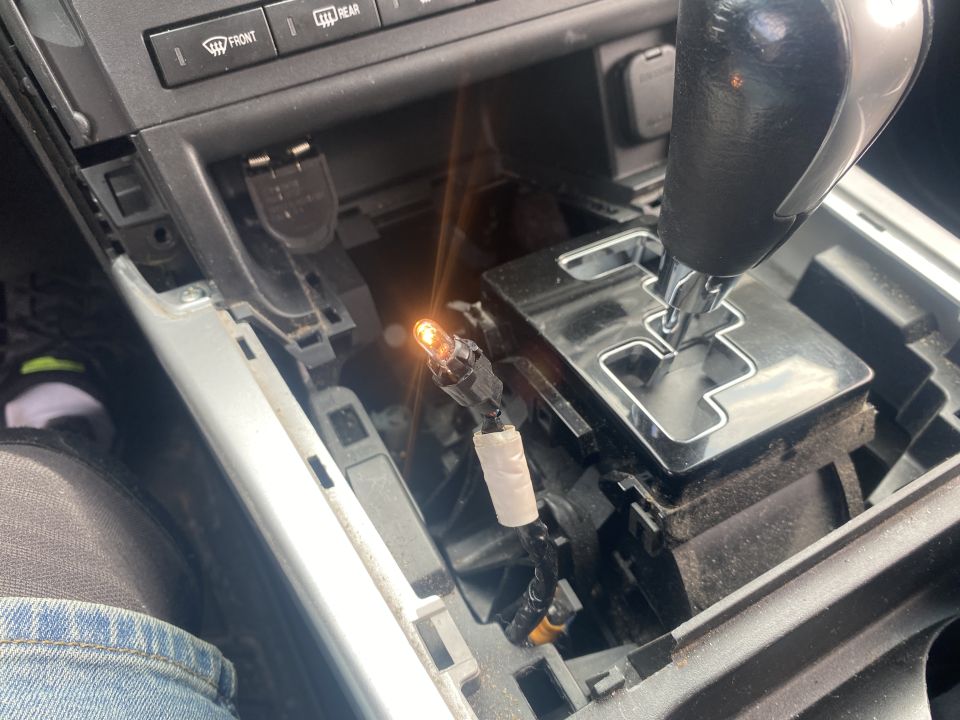 Car center console with gear shifter, partially disassembled, showing an illuminated orange bulb.