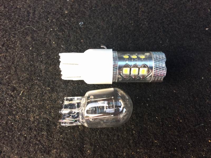Incandescent automotive bulb next to an LED automotive bulb on a dark surface.