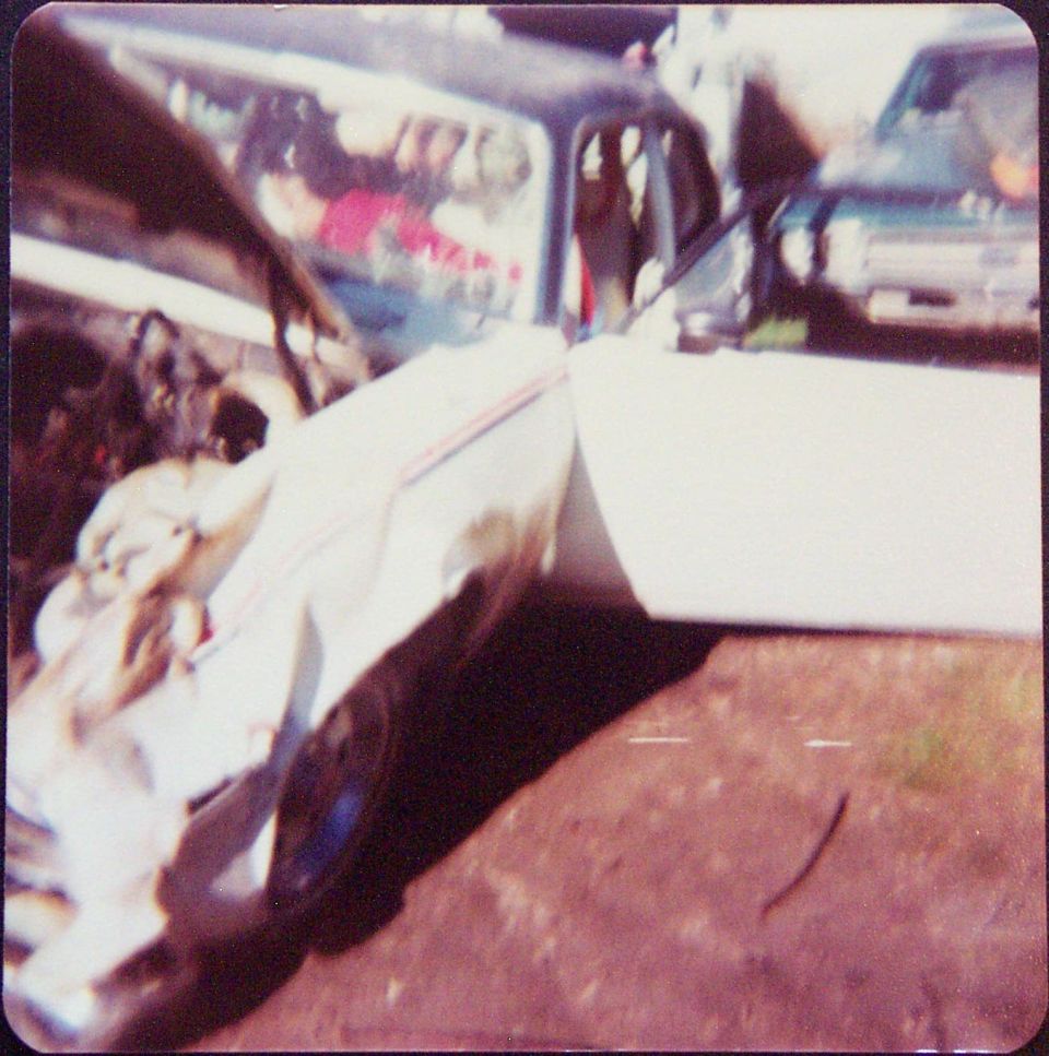 White car with heavy front and side crash damage on dirt lot