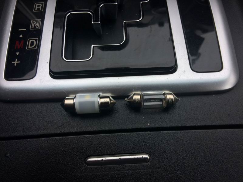 LED bulb next to an incandescent bulb in front of a car's gear shifter.