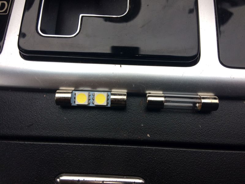 Two glass fuses, one with LED lights, on a dark surface.
