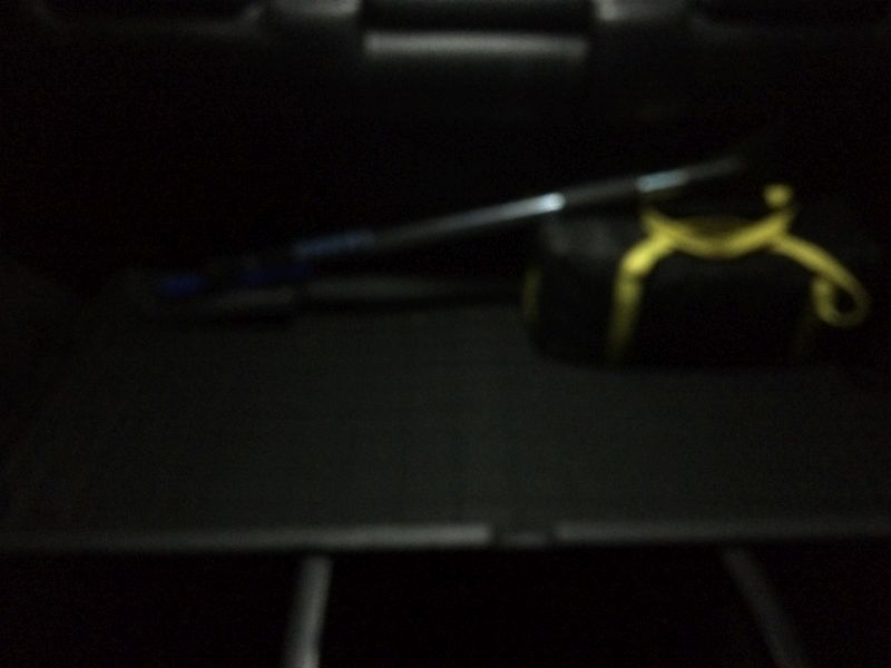Black duffel bag with yellow accents and a long object in a vehicle cargo area.