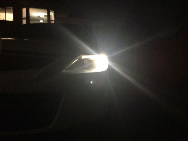 Front view of a white SUV at night with the driver's side headlight on.