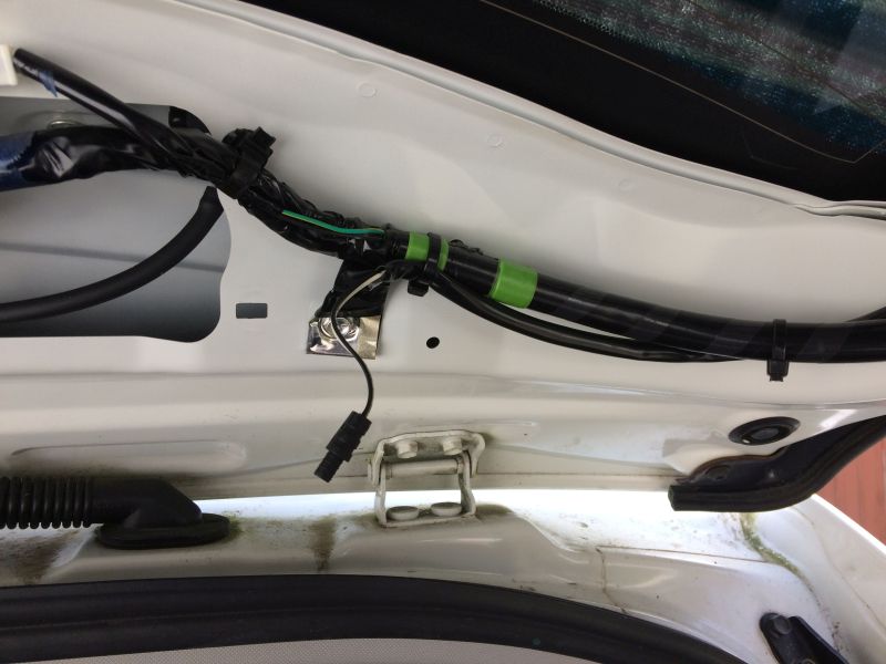 Wiring harness and hinge inside a white vehicle trunk.