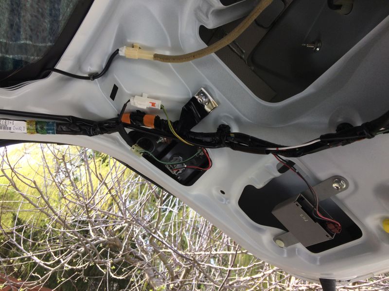 Underside of a car trunk lid showing wiring, connectors, fuse box, and electronic module.