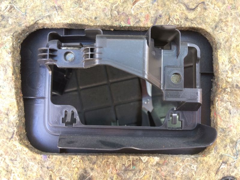 Black plastic bracket assembly inside a cutout of beige sound-dampening material.