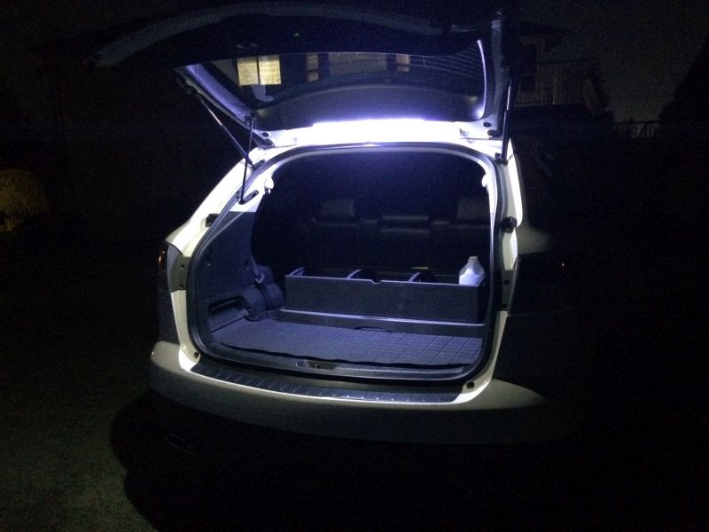 White SUV liftgate open at night, showing illuminated cargo area with organizer and bottle.