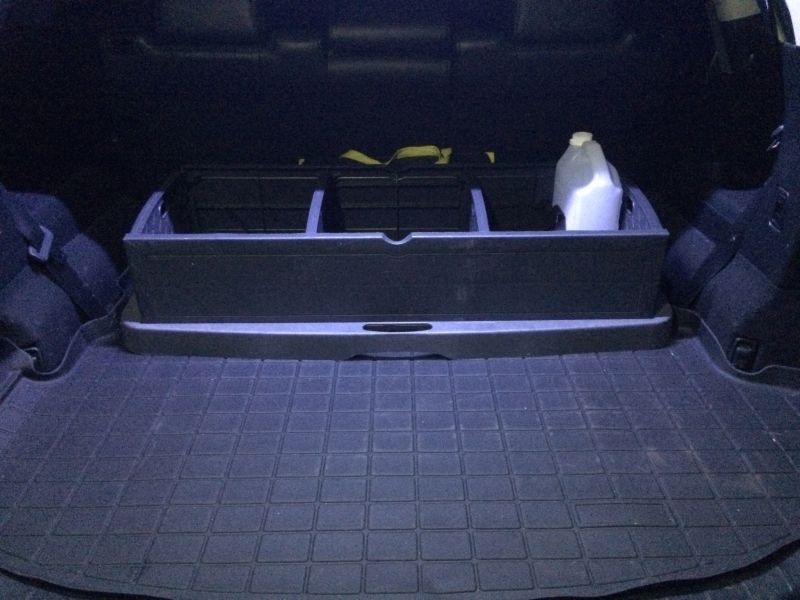 Black cargo organizer and jug in the trunk of a dark SUV with a rubber floor mat.