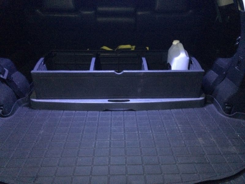 Black plastic cargo organizer with a white jug in the back of a vehicle.
