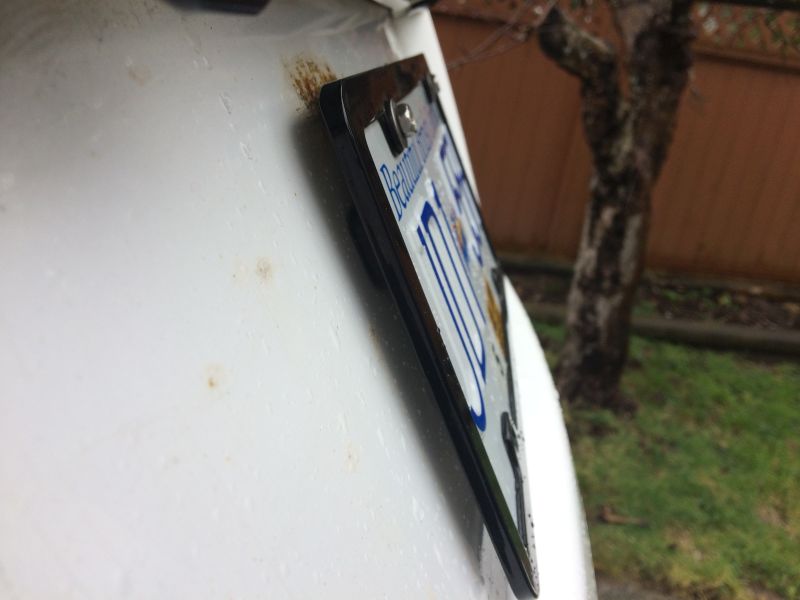 White vehicle rear with license plate, rust spots, and water droplets.