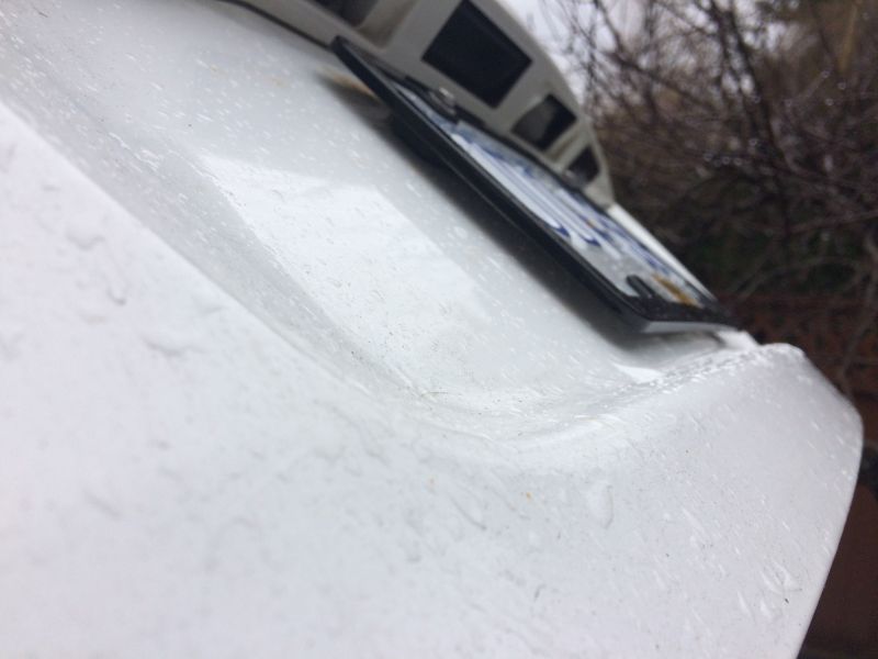 White vehicle rear bumper with license plate frame and water droplets.