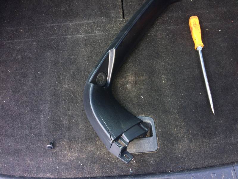 Black plastic car interior trim piece and a yellow screwdriver on dark carpet.