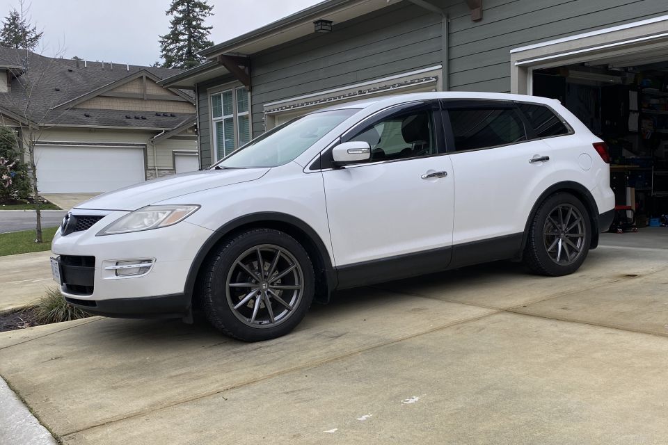 White 2009 Mazda CX-9 SUV with dark gray wheels and window visors parked on a driveway.
