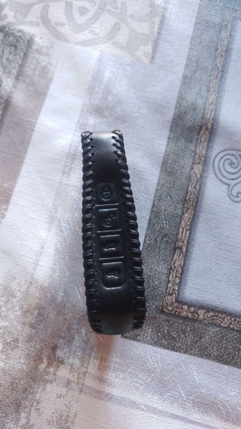 Black leather key fob cover with embossed lock, unlock, and trunk buttons.