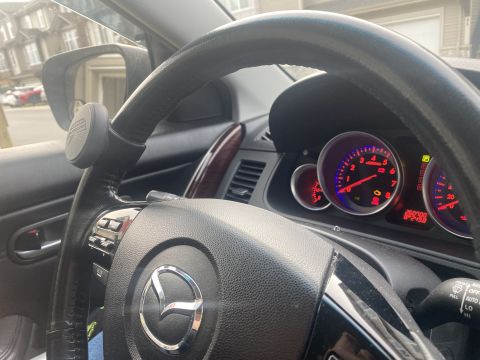 2009 Mazda CX-9 - Close-up interior view of a car's steering wheel and dashboard, showing the Mazda logo on the steering wheel and the instrument cluster wit…