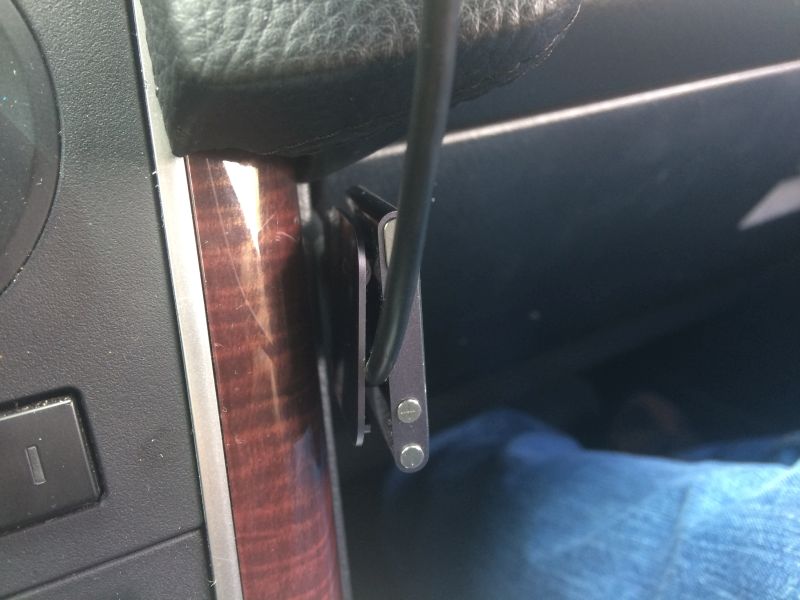 Car interior close-up showing wood trim and a metallic device with a cable attached.