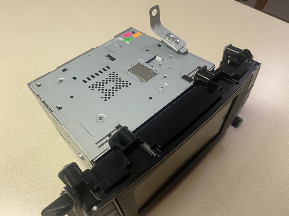 Rear view of a car stereo with metal casing and black faceplate, silver bracket attached.