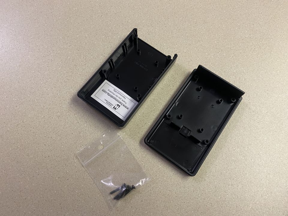 Two black plastic enclosure halves and a bag of screws
