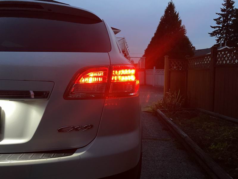 Rear driver's side taillight of a silver SUV illuminated at dusk.