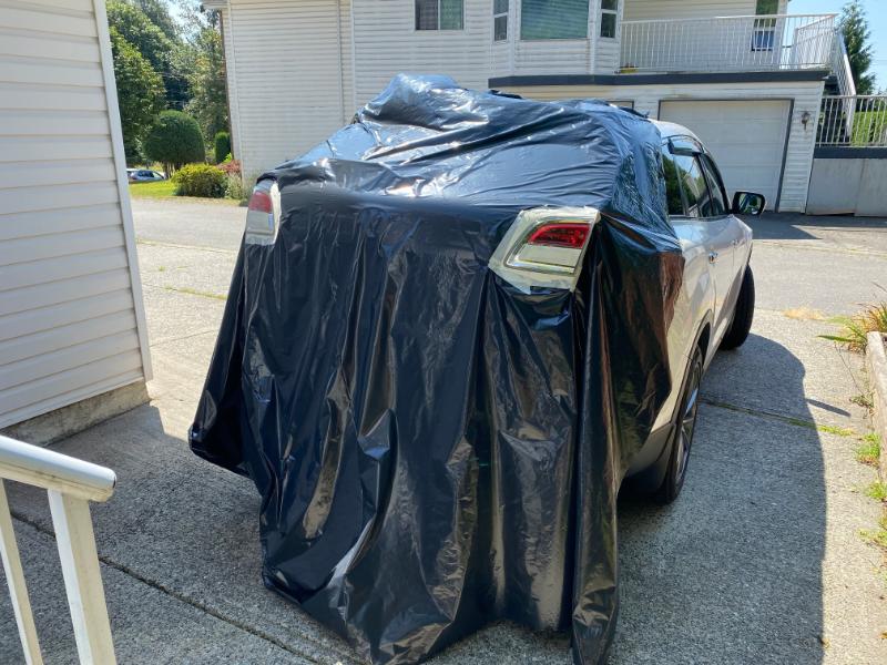 White SUV covered by a black tarp, showing the rear taillight.