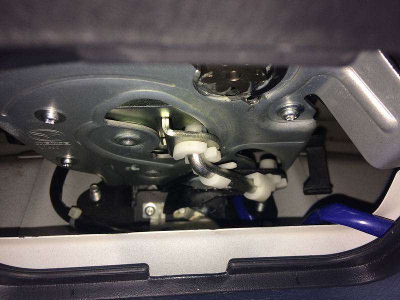 Close-up of car trunk latch mechanism with metal parts, wires, and plastic connectors.