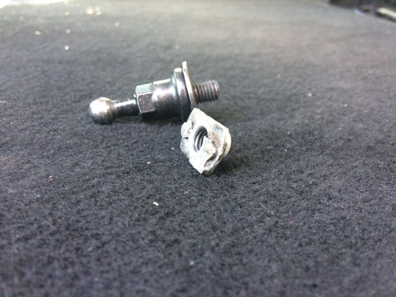Broken metal ball stud and nut on a dark textured surface.
