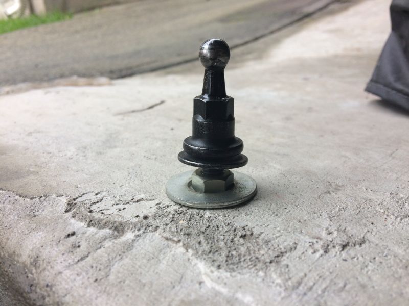 Black shifter knob with ball top on a bolt with washers and nut on concrete.