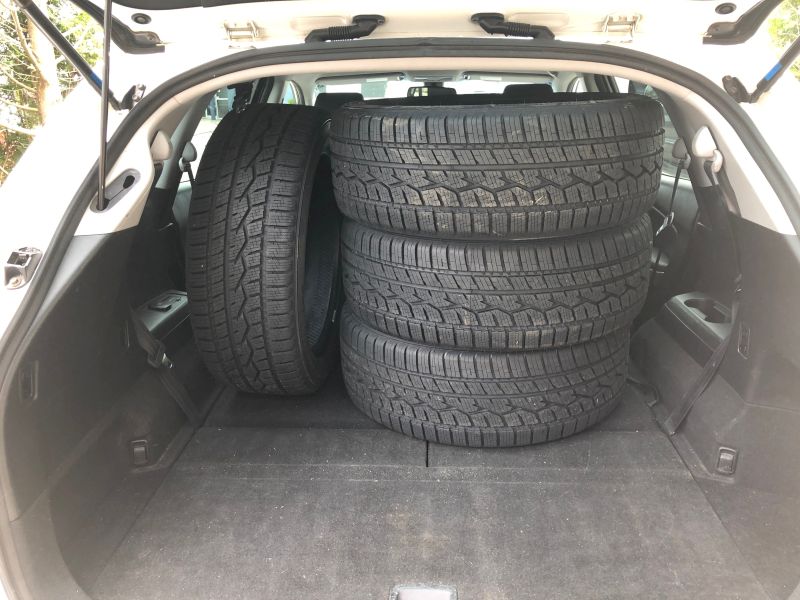 Four black winter tires stacked in the open trunk of a white SUV.